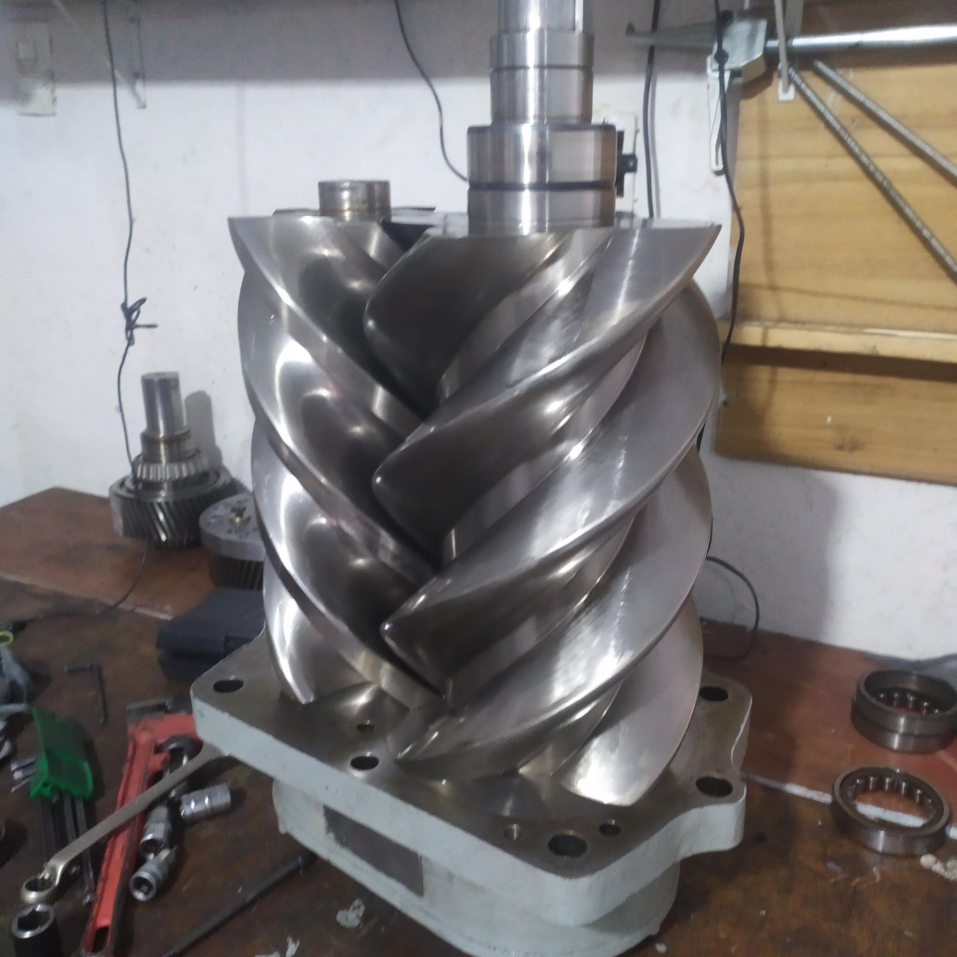 Close-up of a shiny metal screw rotor on a workbench with tools in the background.